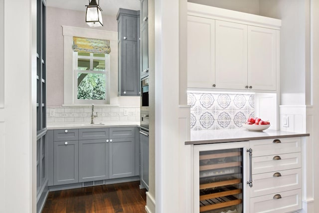 bar featuring beverage cooler, a sink, dark wood finished floors, backsplash, and pendant lighting
