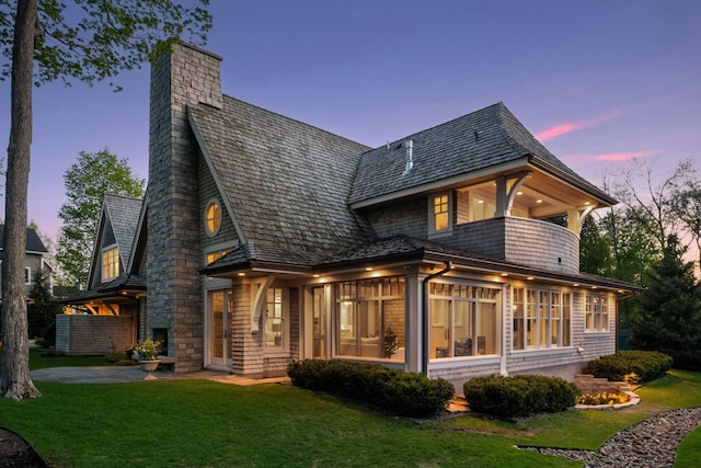 back of property featuring a balcony, a chimney, a lawn, and a sunroom