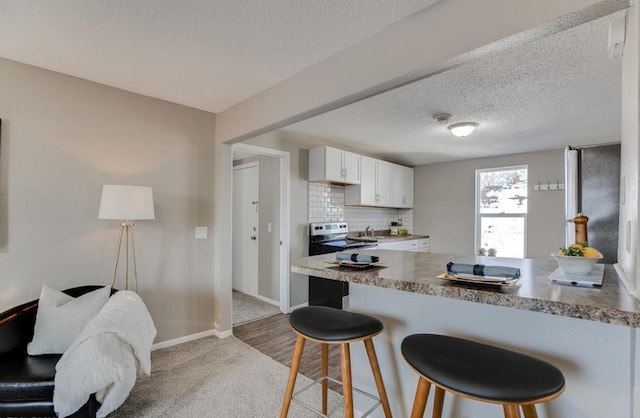 kitchen with stainless steel electric stove, light hardwood / wood-style flooring, decorative backsplash, white cabinetry, and a breakfast bar area