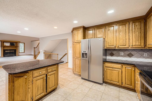 kitchen featuring appliances with stainless steel finishes, tasteful backsplash, dark stone counters, light tile patterned floors, and a textured ceiling