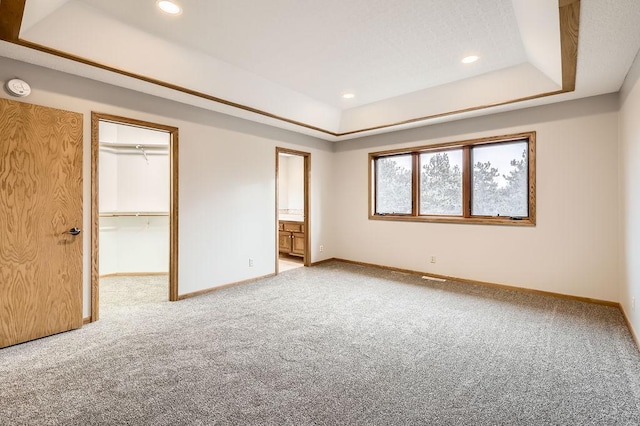 unfurnished bedroom with connected bathroom, a tray ceiling, carpet, and a spacious closet