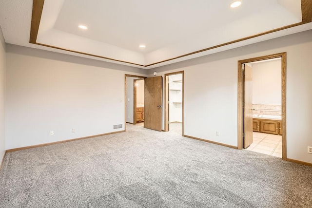 unfurnished bedroom with a walk in closet, light colored carpet, and a tray ceiling