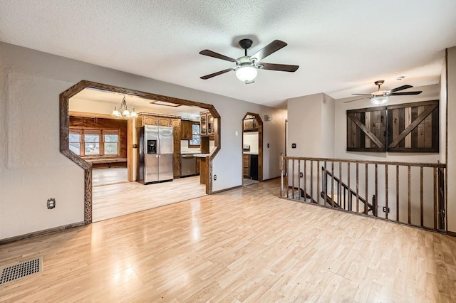 living room featuring ceiling fan with notable chandelier, light hardwood / wood-style flooring, and a textured ceiling