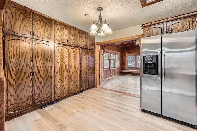 kitchen featuring wood walls, decorative light fixtures, stainless steel refrigerator with ice dispenser, a textured ceiling, and light hardwood / wood-style flooring