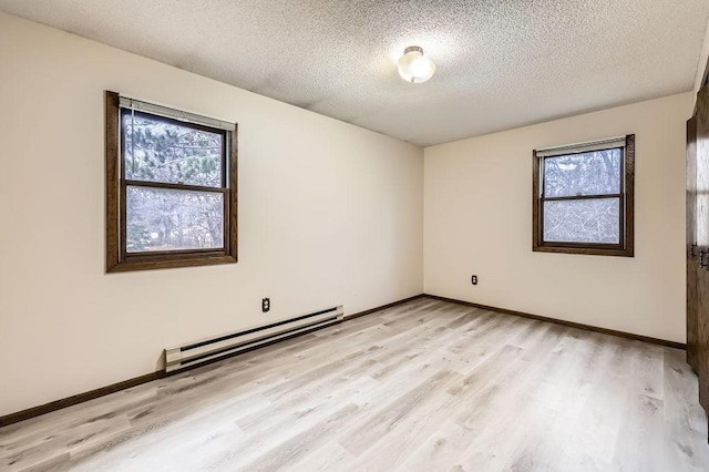 empty room featuring plenty of natural light, light hardwood / wood-style floors, a textured ceiling, and baseboard heating