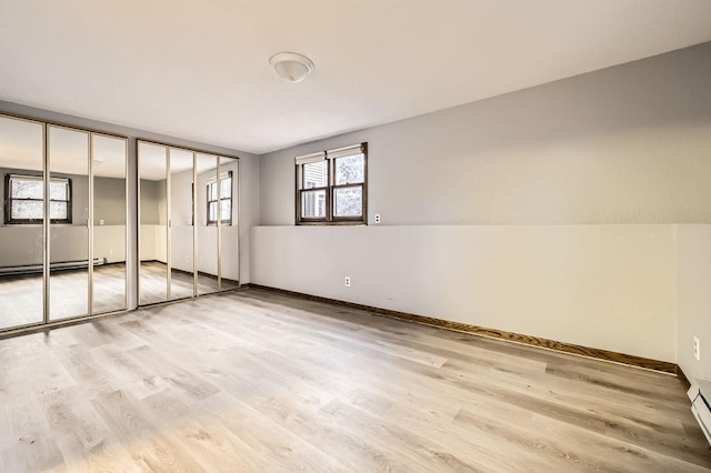 unfurnished bedroom featuring multiple closets, a baseboard radiator, and light hardwood / wood-style flooring