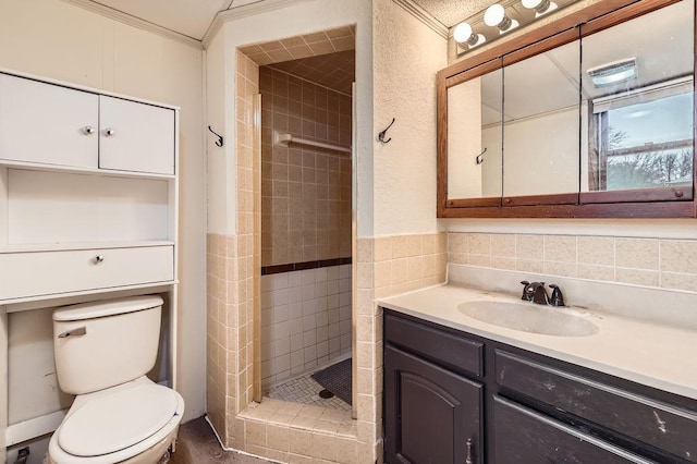 bathroom with vanity, ornamental molding, toilet, and tiled shower