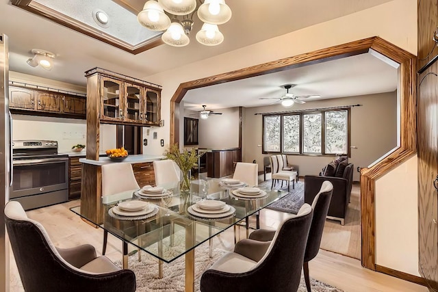 dining space with ceiling fan with notable chandelier and light wood-type flooring