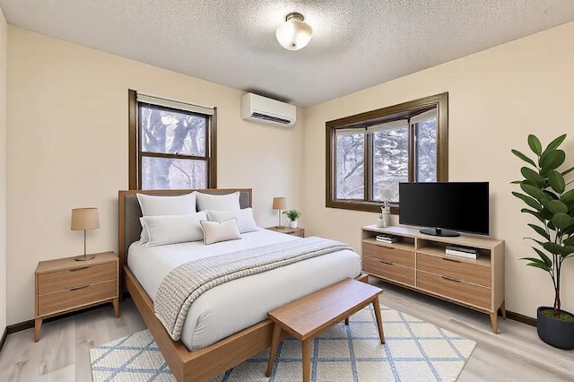 bedroom with a textured ceiling, a wall unit AC, and light wood-type flooring