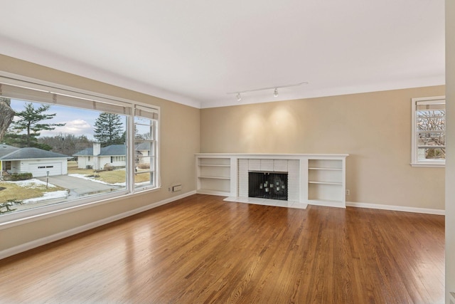 unfurnished living room with a brick fireplace, track lighting, baseboards, and wood finished floors