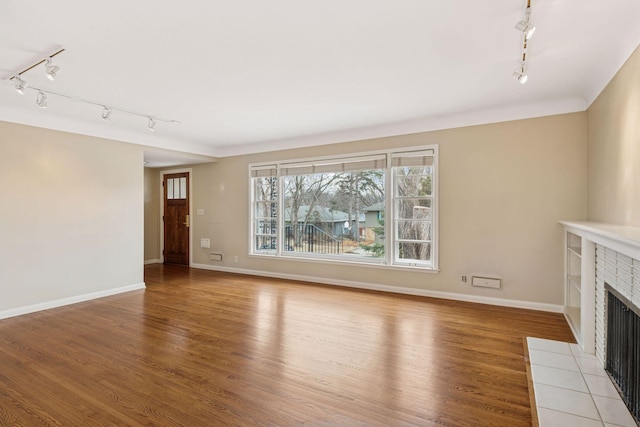 unfurnished living room with baseboards, light wood finished floors, and a tiled fireplace