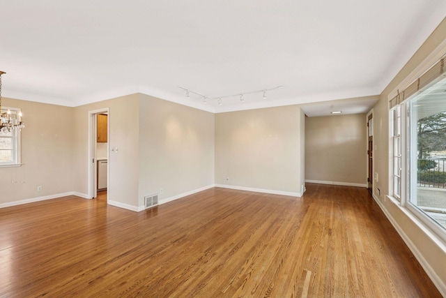 empty room with an inviting chandelier, baseboards, visible vents, and light wood-style floors