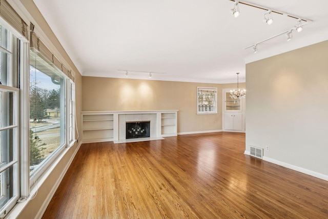 unfurnished living room featuring a chandelier, wood finished floors, visible vents, baseboards, and a brick fireplace