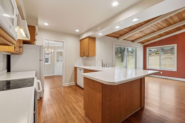 kitchen with white appliances, light wood finished floors, a peninsula, vaulted ceiling with beams, and a sink