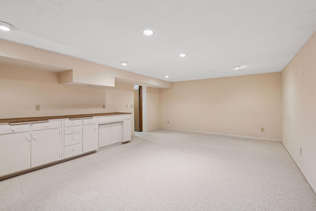 kitchen featuring light carpet, baseboards, white cabinets, a textured ceiling, and recessed lighting