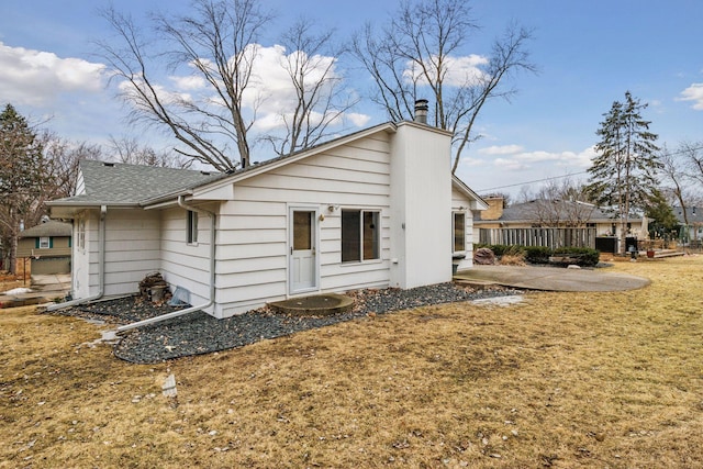 back of house featuring a patio area, a shingled roof, a chimney, and a yard