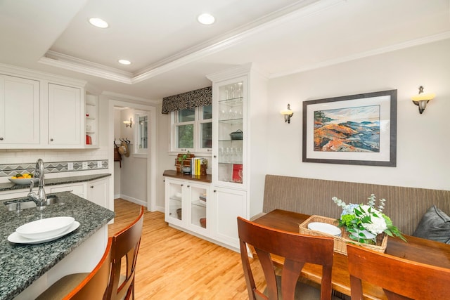 kitchen with tasteful backsplash, dark stone counters, light hardwood / wood-style floors, a tray ceiling, and white cabinets