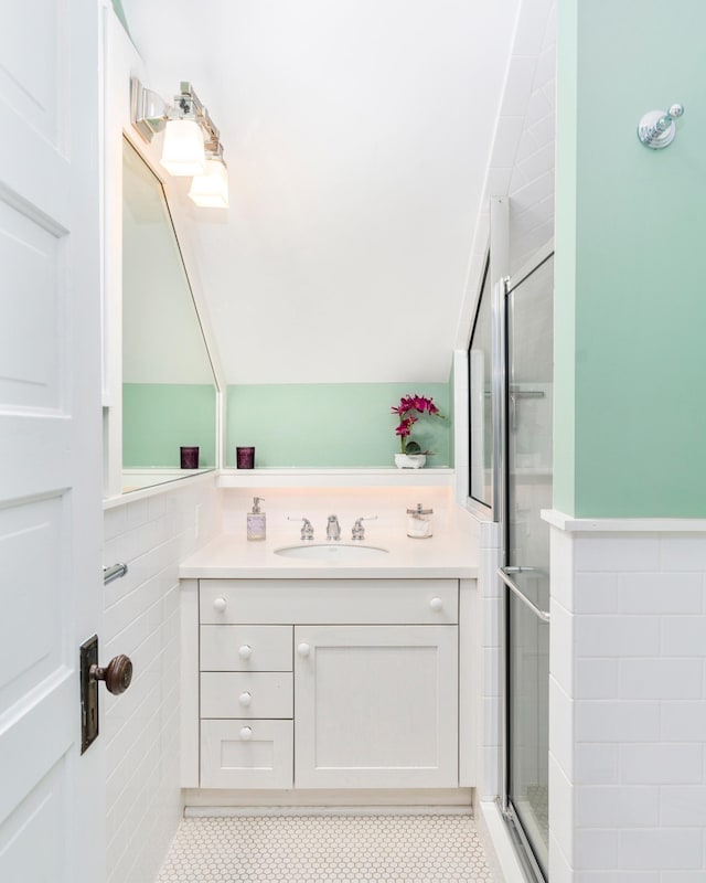 bathroom with tile patterned floors, tile walls, a shower with shower door, and sink