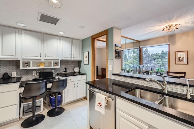 kitchen featuring visible vents, dark countertops, stainless steel dishwasher, white cabinetry, and a sink