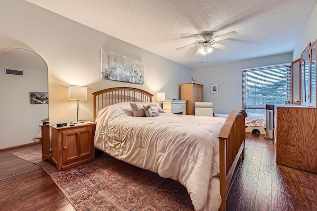 bedroom with arched walkways, visible vents, dark wood-type flooring, a ceiling fan, and a textured ceiling