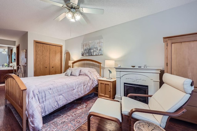 bedroom featuring a textured ceiling, ceiling fan, dark wood finished floors, a closet, and a glass covered fireplace