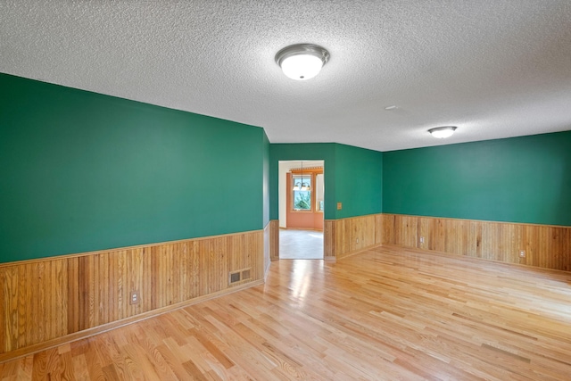 empty room with a textured ceiling, light hardwood / wood-style floors, and wooden walls