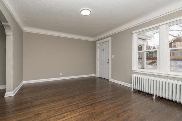 spare room with a textured ceiling, radiator heating unit, dark wood-type flooring, and ornamental molding