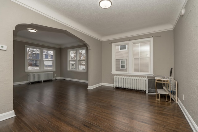 empty room with a textured ceiling, dark hardwood / wood-style flooring, radiator, and ornamental molding