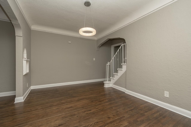 empty room with a textured ceiling, crown molding, and dark wood-type flooring