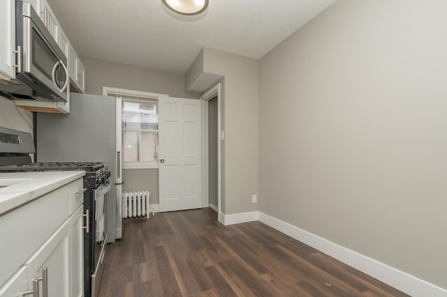 kitchen featuring radiator, white cabinetry, stainless steel appliances, and dark hardwood / wood-style floors