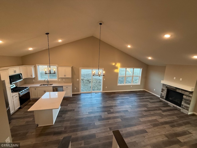 kitchen with appliances with stainless steel finishes, a kitchen island, pendant lighting, white cabinets, and a stone fireplace