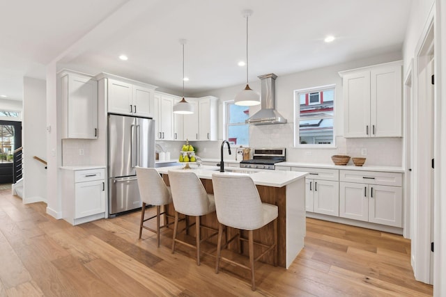 kitchen featuring white cabinets, stainless steel appliances, wall chimney range hood, and light wood-type flooring