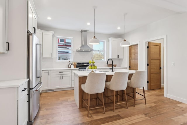 kitchen with a center island with sink, white cabinetry, wall chimney exhaust hood, and light hardwood / wood-style flooring