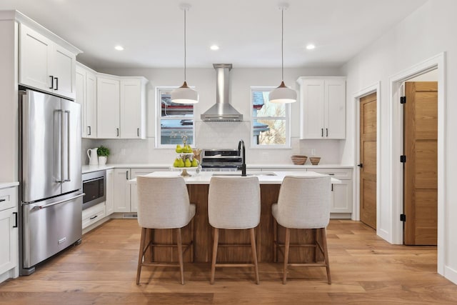 kitchen with wall chimney exhaust hood, white cabinetry, appliances with stainless steel finishes, and light hardwood / wood-style flooring