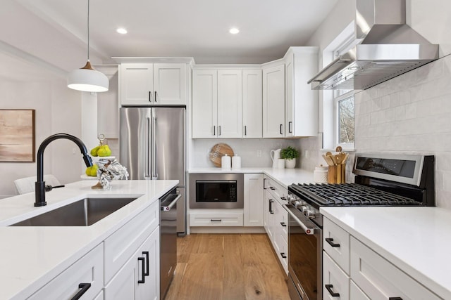 kitchen featuring sink, wall chimney range hood, pendant lighting, white cabinets, and appliances with stainless steel finishes