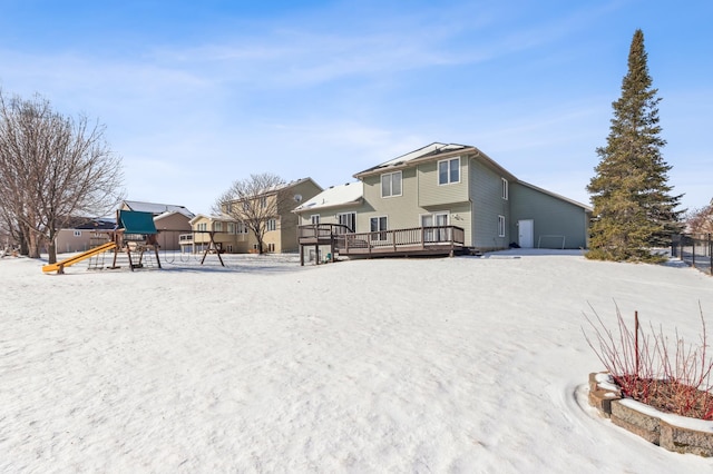 snowy yard featuring a wooden deck and a playground