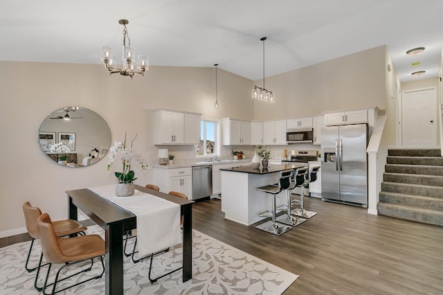 dining room featuring ceiling fan with notable chandelier, sink, dark wood-type flooring, and high vaulted ceiling