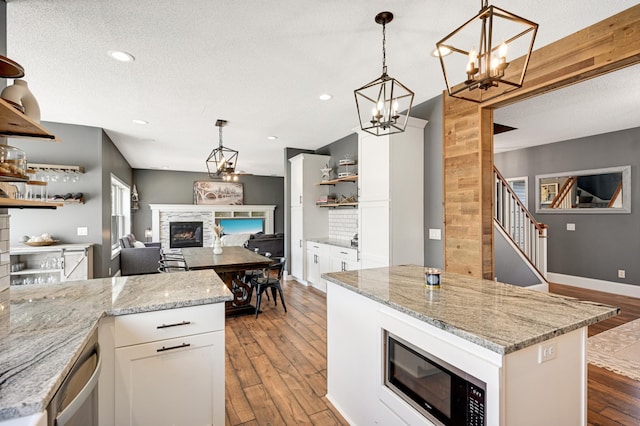 kitchen featuring built in microwave, white cabinetry, a stone fireplace, light stone counters, and light wood-type flooring