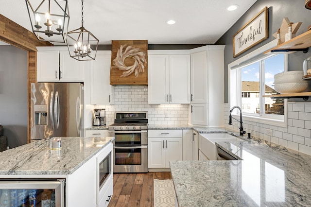 kitchen with sink, stainless steel appliances, decorative light fixtures, white cabinets, and hardwood / wood-style flooring