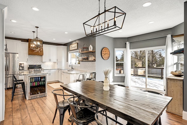 dining room featuring wine cooler, a wealth of natural light, light hardwood / wood-style flooring, and a textured ceiling