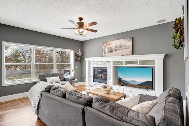 living room with a stone fireplace, ceiling fan, wood-type flooring, and a textured ceiling