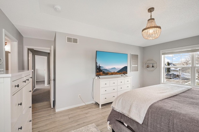 bedroom with a chandelier, a textured ceiling, and light hardwood / wood-style floors