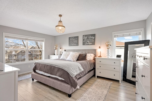 bedroom with a textured ceiling, a notable chandelier, and light wood-type flooring