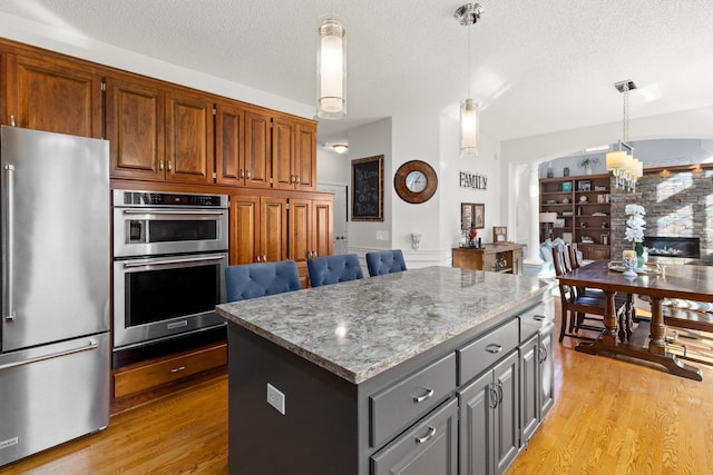 kitchen featuring light wood finished floors, hanging light fixtures, gray cabinetry, appliances with stainless steel finishes, and a kitchen island