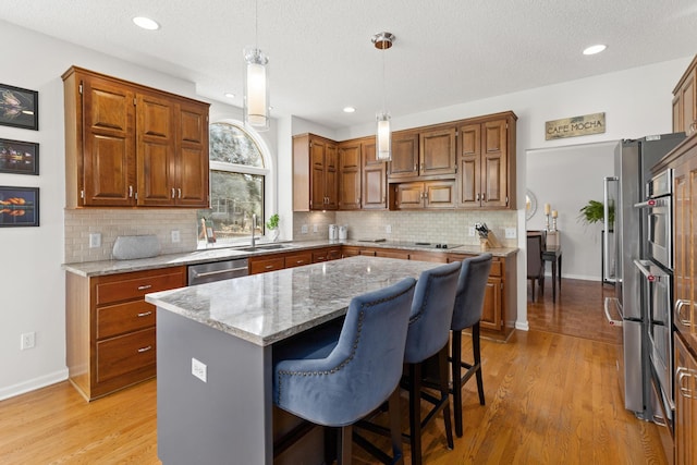 kitchen with a center island, brown cabinets, decorative light fixtures, a sink, and light stone countertops