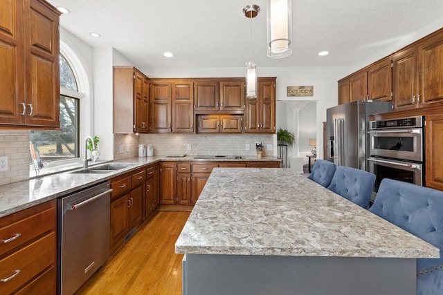 kitchen featuring a center island, pendant lighting, appliances with stainless steel finishes, light wood-style floors, and a sink