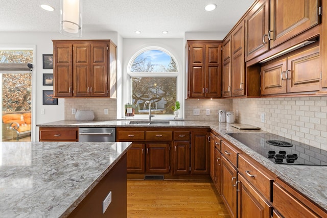 kitchen featuring light stone counters, light wood-style floors, brown cabinetry, a sink, and dishwasher