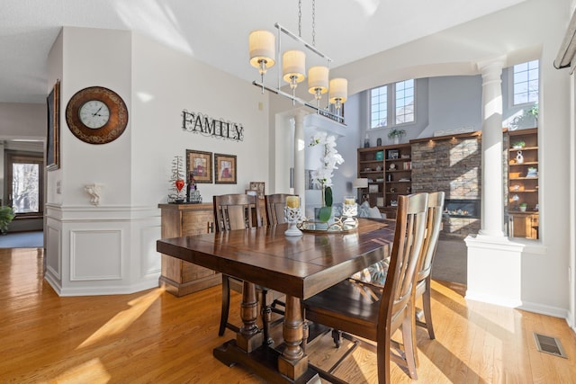 dining area with ornate columns, visible vents, light wood finished floors, and a wainscoted wall