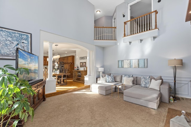 living area featuring a towering ceiling, decorative columns, arched walkways, and carpet flooring