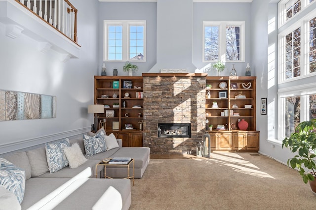 carpeted living area featuring a healthy amount of sunlight, a stone fireplace, and a high ceiling